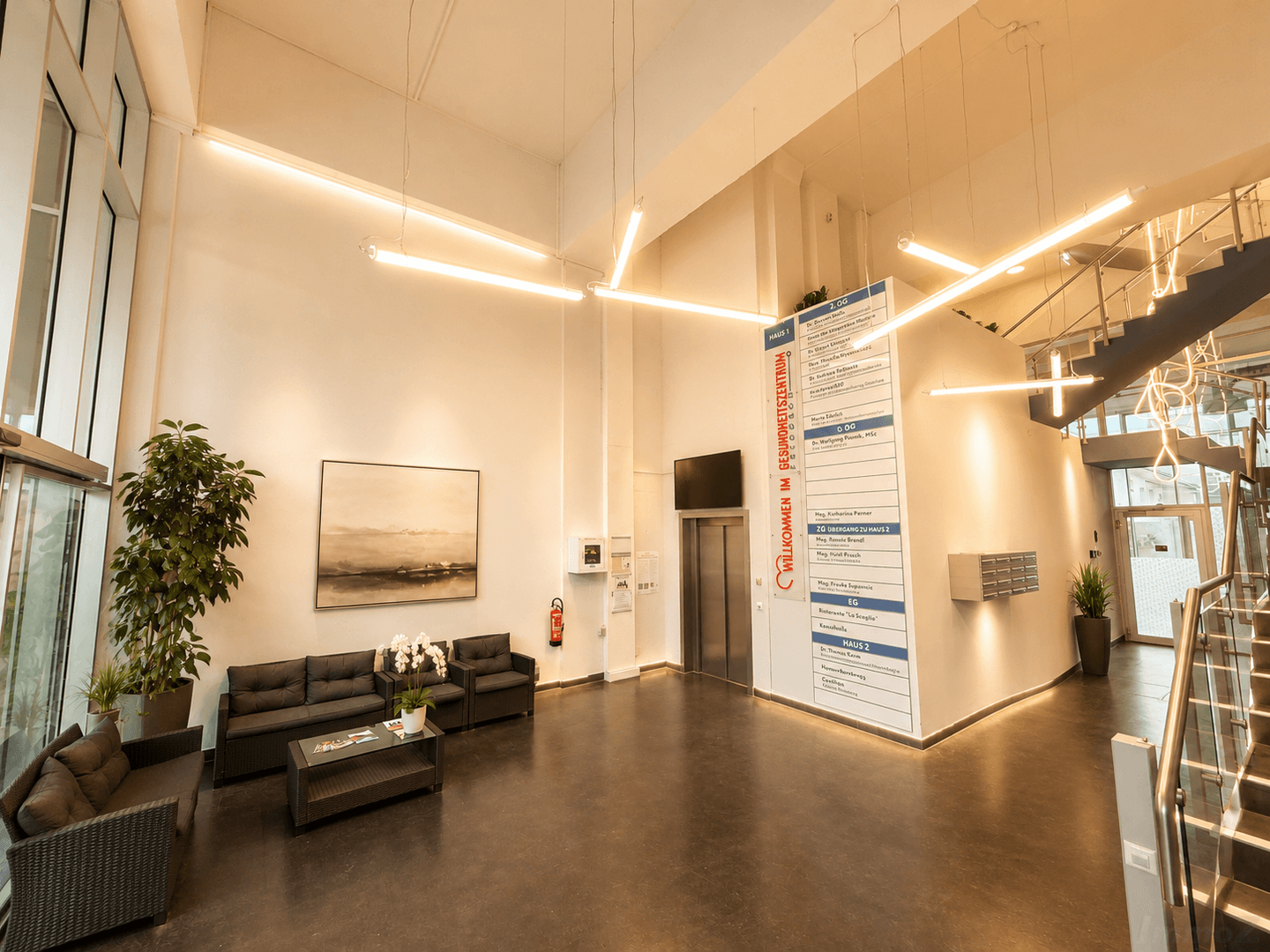Geräumige und moderne Lobby eines Gesundheitszentrums mit hohen Decken, bequemen Sitzgelegenheiten und Aufzug.