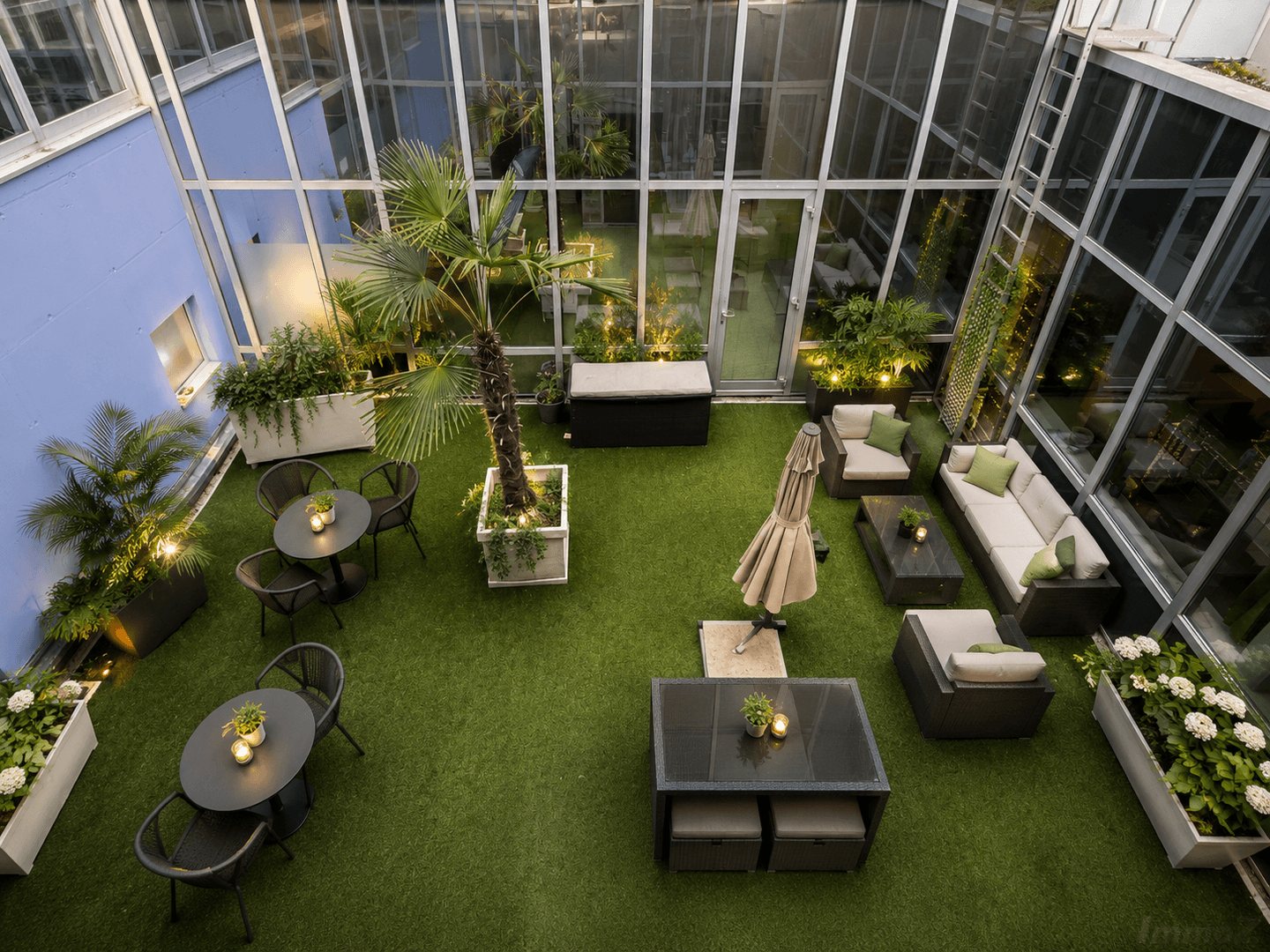 Attraktive Dachterrasse mit Kunstrasen, bequemen Gartenmöbeln und Pflanzen, umgeben von Glasfassaden.