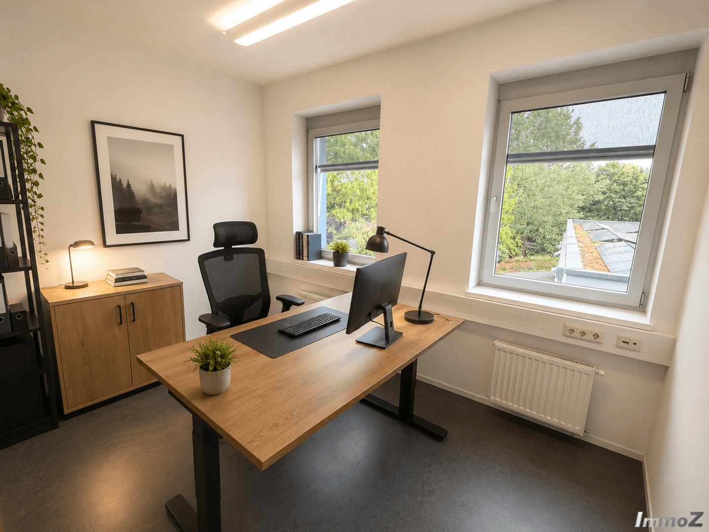 Helles Büro mit Schreibtisch, Bürostuhl und zwei Fenstern mit Blick ins Grüne.