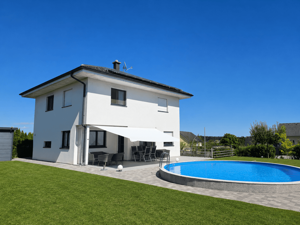Modernes Einfamilienhaus mit weißer Fassade, großem Garten und ovalem Aufstellpool.