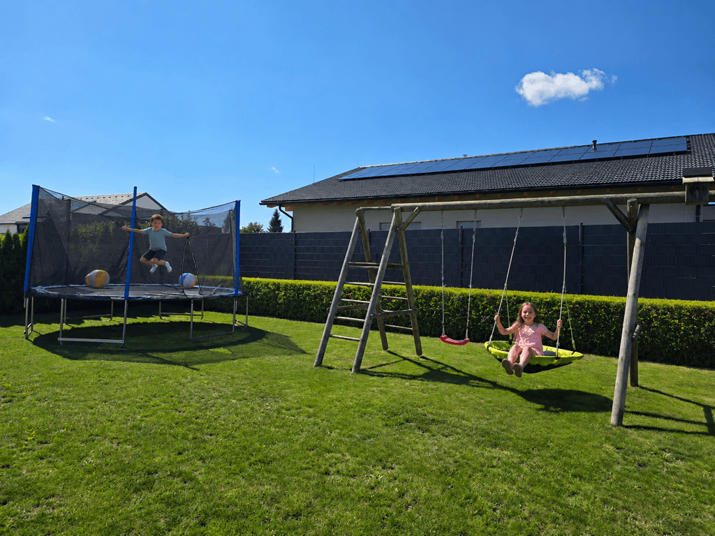 Großer Gartenbereich mit Trampolin und Schaukel für Kinder unter blauem Himmel.