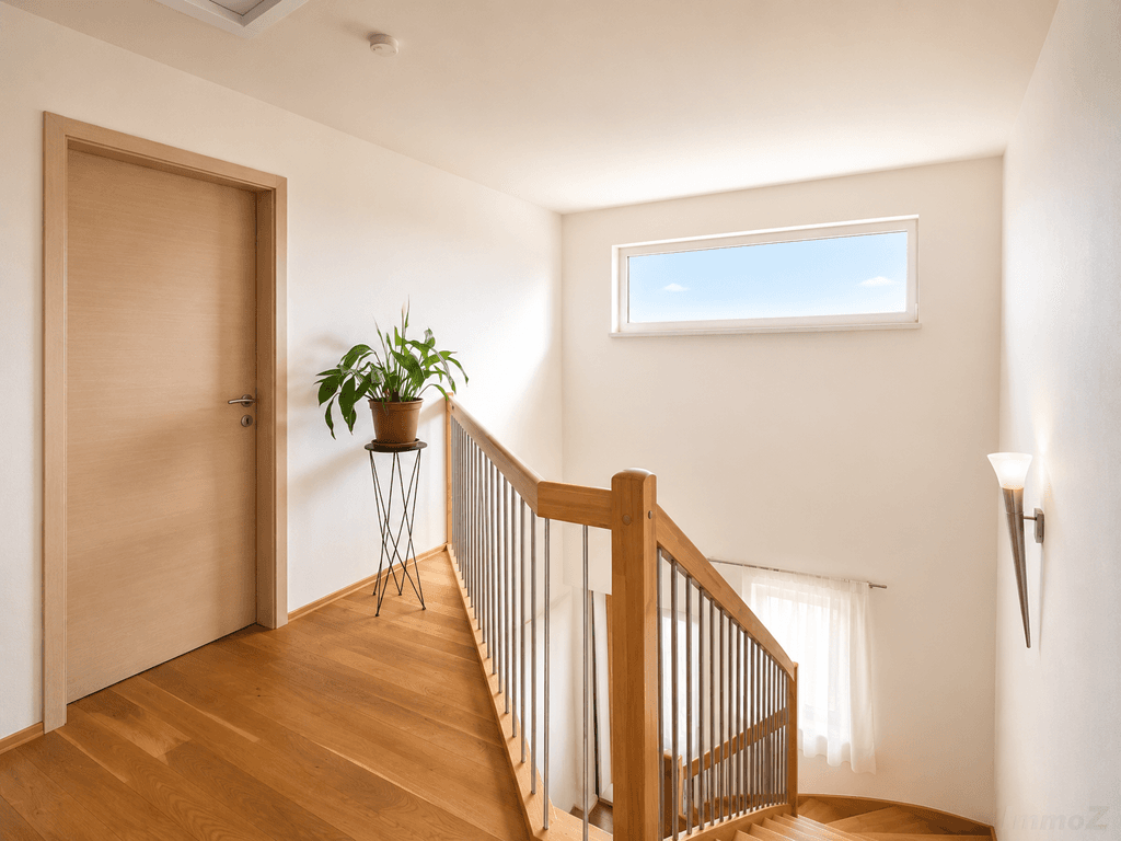 Heller Treppenaufgang mit Holztreppe, Edelstahlgeländer und Fenster für natürliches Licht.