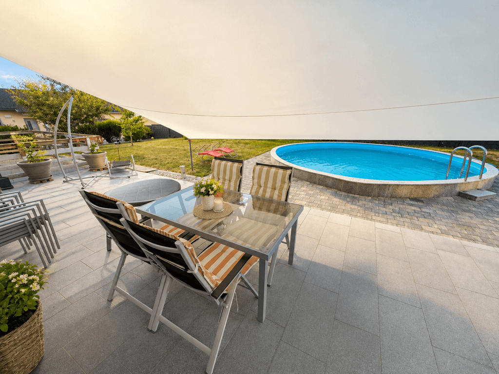 Gemütliche Terrasse mit Esstisch, Sonnensegel und Blick auf den Pool im Garten.