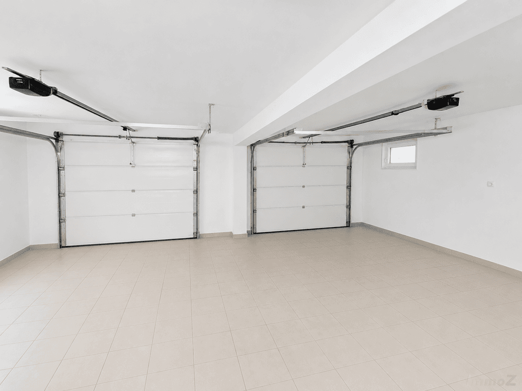 Geräumige Doppelgarage mit zwei Sektionaltoren und Fliesenboden.