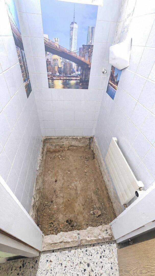Kleiner Raum im Rohbauzustand mit gefliesten Wänden, Erdboden und Heizkörper, bereit für den Ausbau.