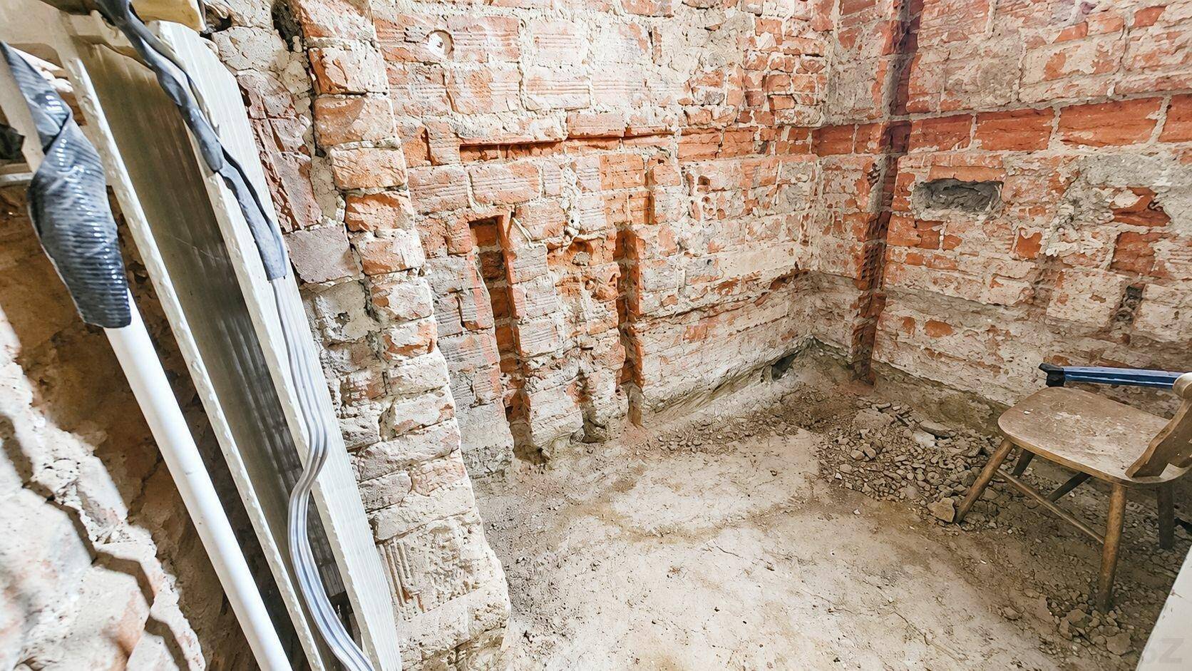 Rohbauzustand eines Raumes mit freigelegten Ziegelwänden und Erdboden, bereit für den Ausbau.