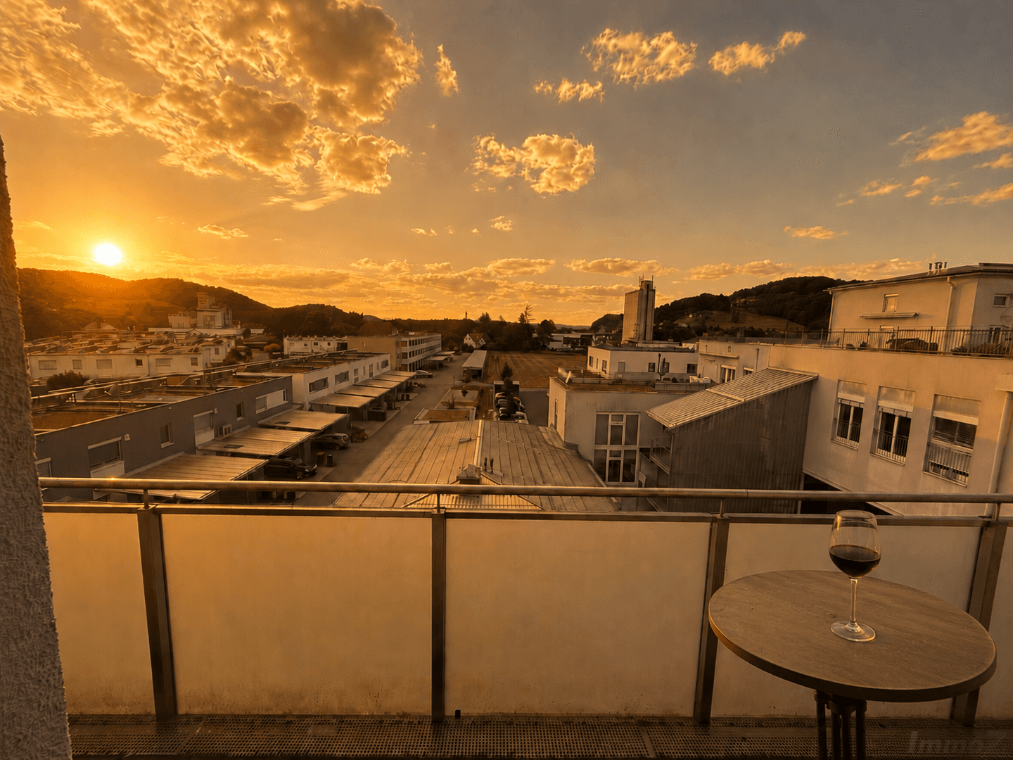 Balkon bei Sonnenuntergang mit einem Glas Wein und weitem Blick über die Stadt und die umliegenden Hügel.