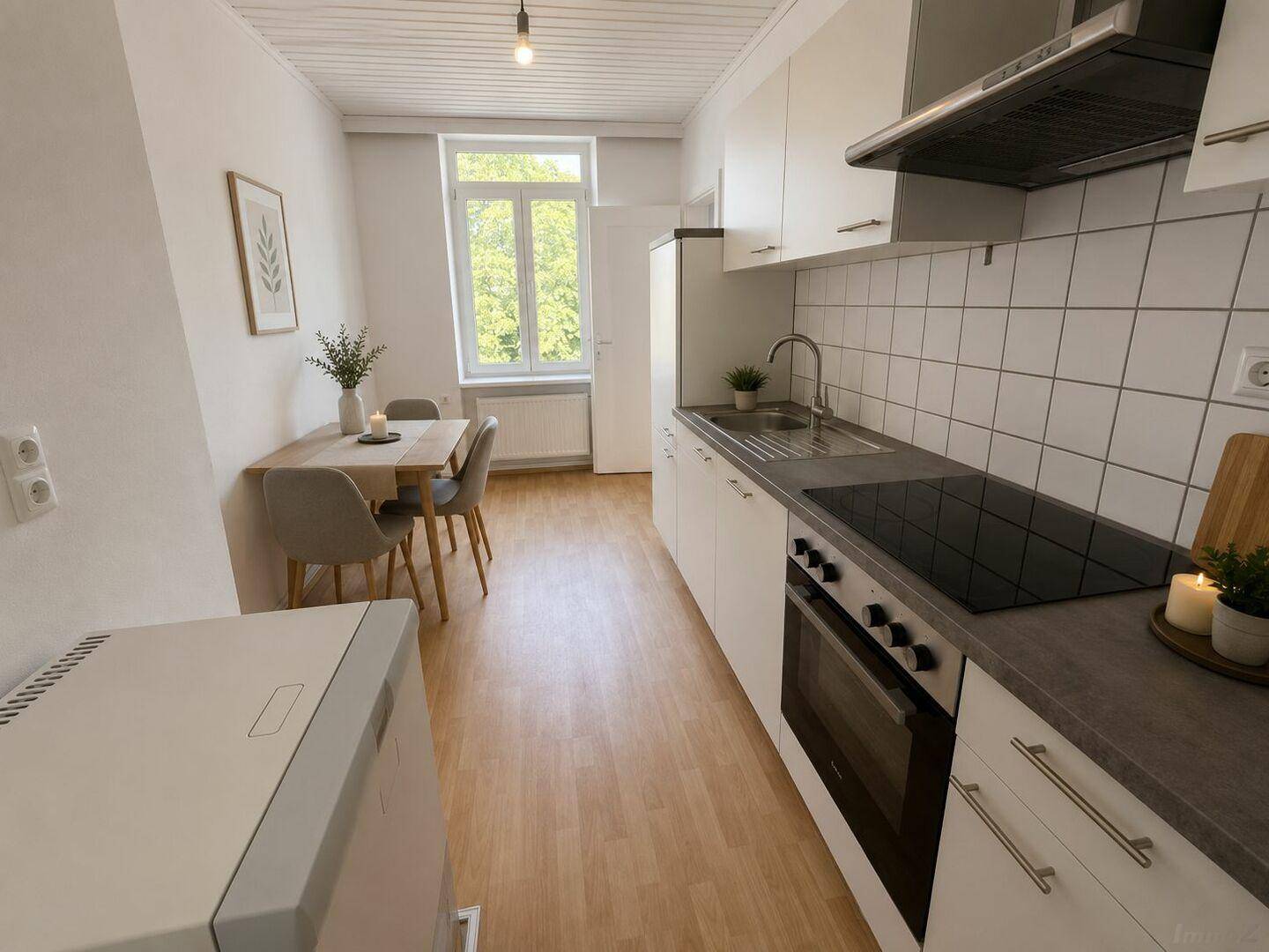 Moderne Küche mit weißen Schränken, Induktionskochfeld und Essbereich am Fenster.