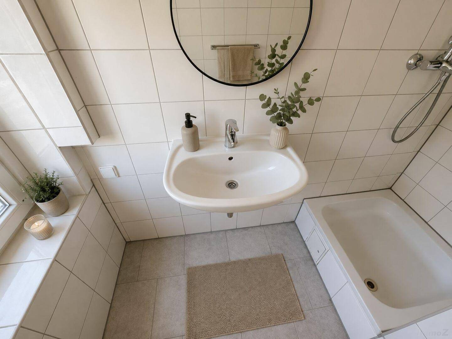 Modernes Badezimmer mit weißen Fliesen, Waschbecken, rundem Spiegel und Badewanne mit Duschfunktion.