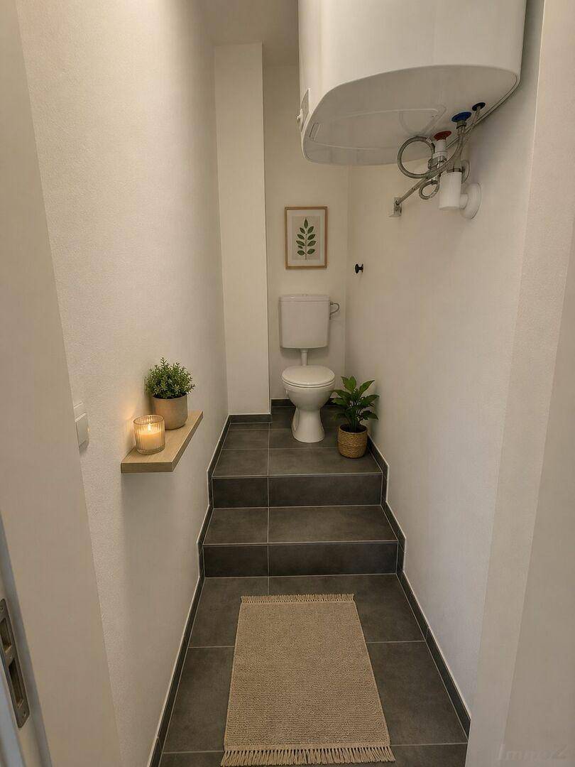 Kleines WC mit dunklen Fliesen und Wandtoilette, ausgestattet mit einem Warmwasserboiler.