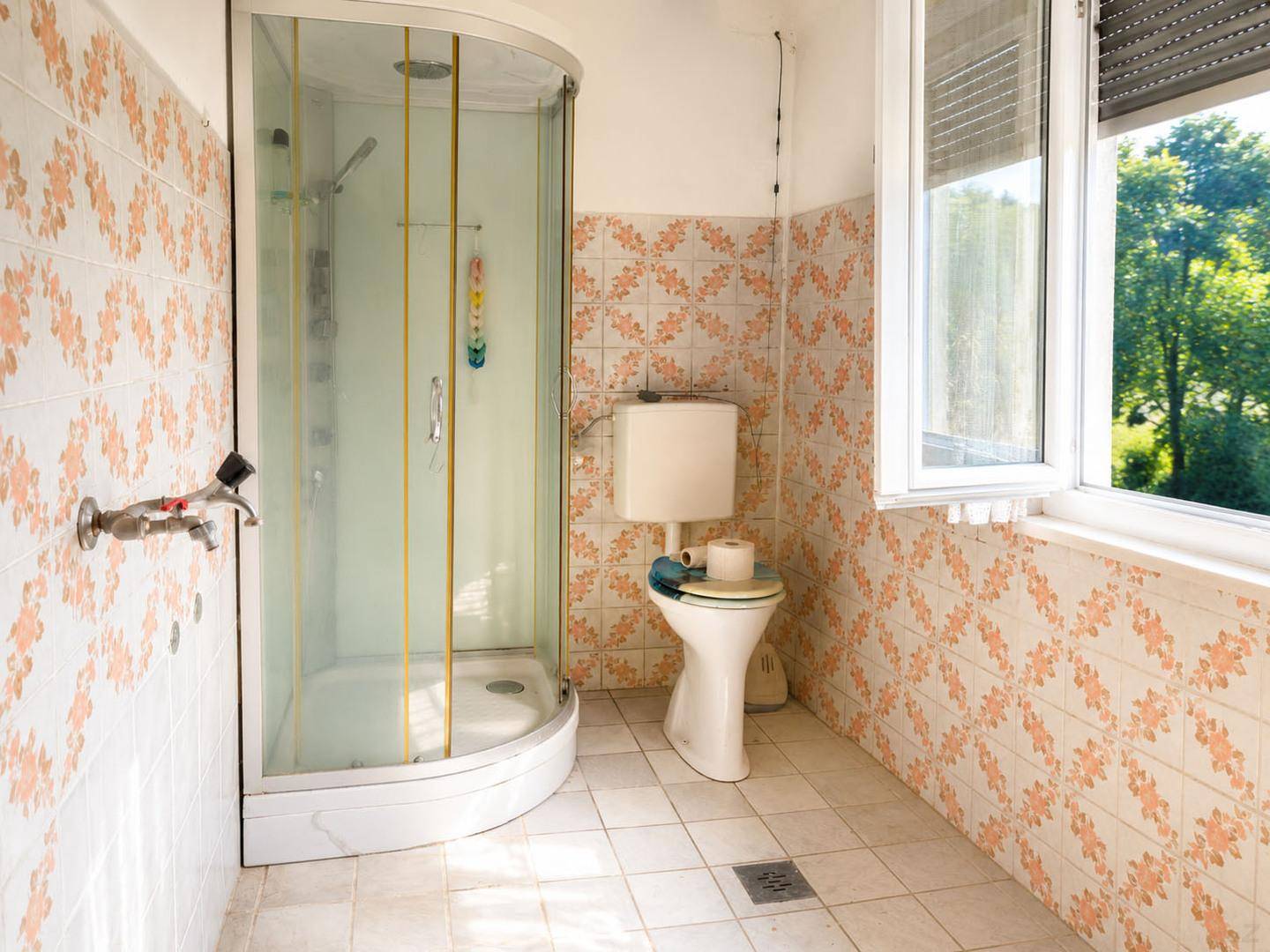 Badezimmer mit Duschkabine, Toilette und gemusterten Fliesen, hell durch ein Fenster.