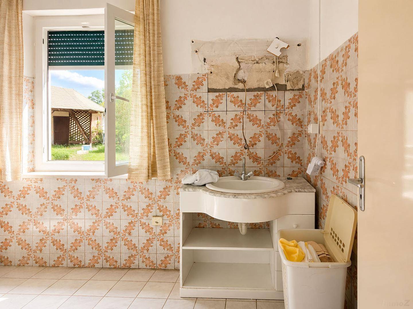 Badezimmer mit Waschbecken, alten gemusterten Fliesen und Fenster mit Blick nach draußen.