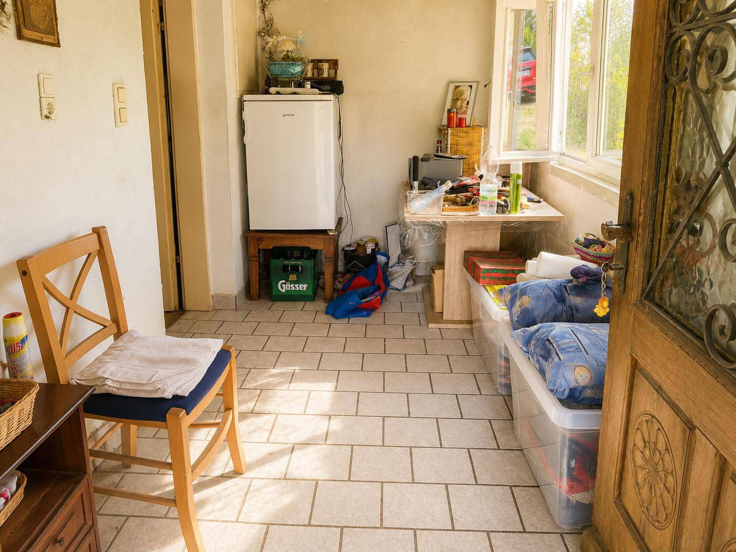 Heller Wintergarten oder verglaster Vorraum mit Fliesenboden und Blick ins Grüne, als Abstellraum genutzt.