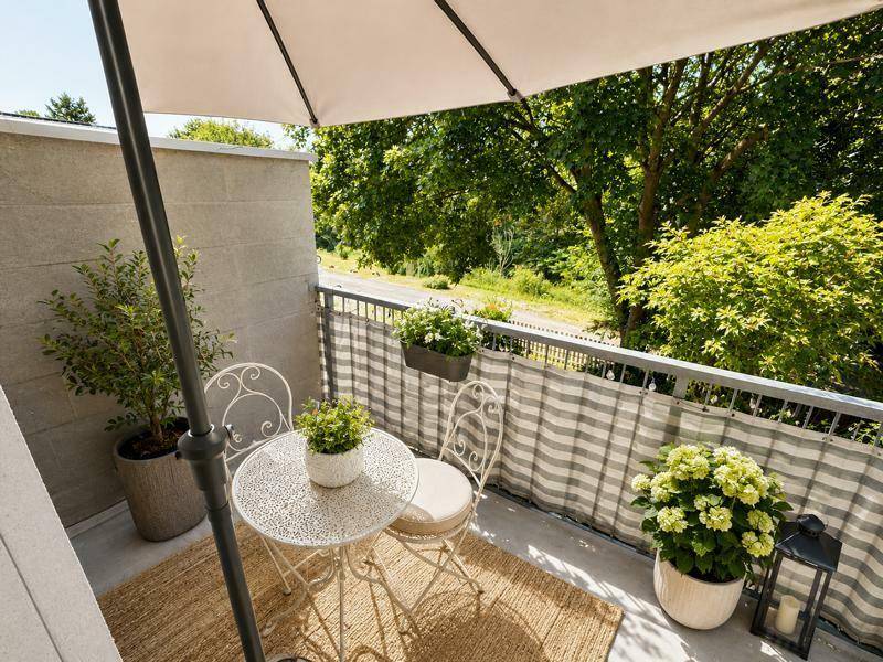 Kleiner Balkon mit Sitzgelegenheit, Sonnenschirm und Blick auf Bäume und die Umgebung.
