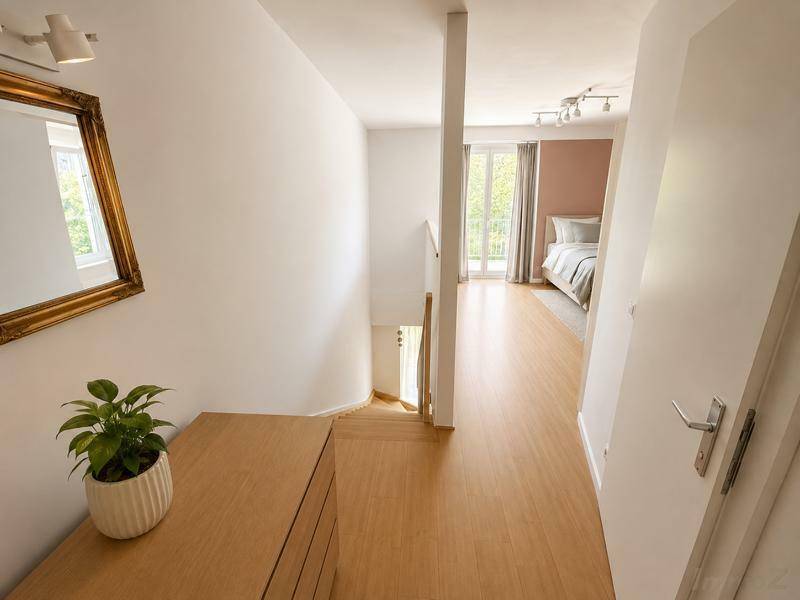 Heller Flur mit Holzboden, Spiegel und Blick in ein weiteres Zimmer mit Balkonzugang.