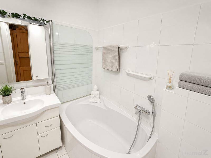 Modernes Badezimmer mit weißen Fliesen, Einzelwaschbecken und Eckbadewanne mit Duschabtrennung.
