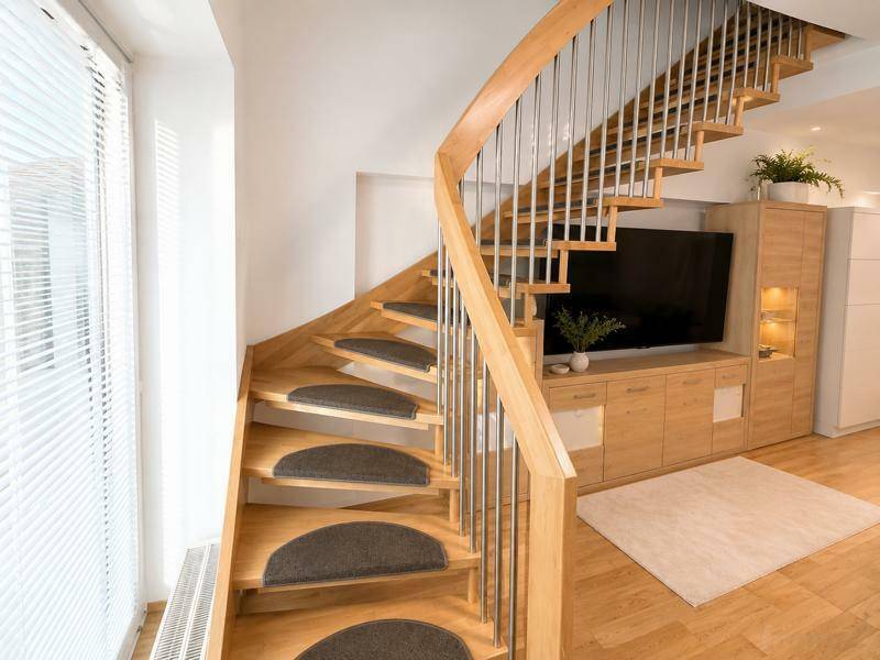 Elegante Holztreppe mit Metallgeländer und Blick auf den Wohnbereich mit TV-Möbeln.