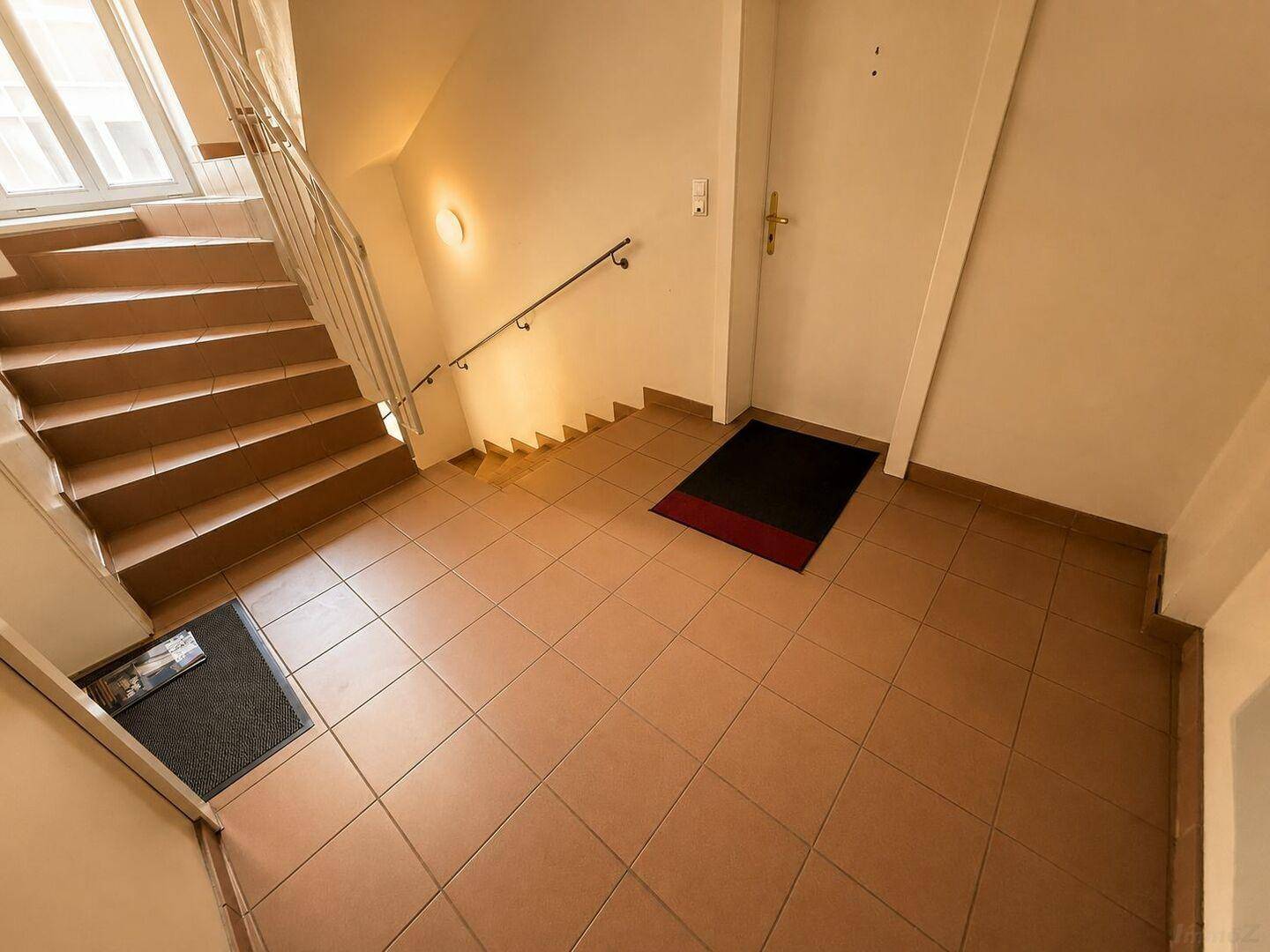 Helles Treppenhaus mit Fliesenboden und einem Fenster, das für natürliches Licht sorgt.