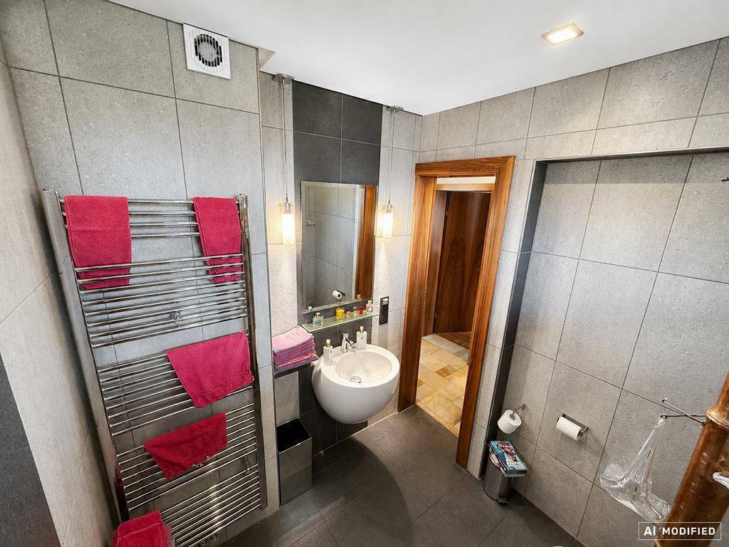 Modernes Badezimmer mit grauen Fliesen, ovalem Waschbecken und beheiztem Handtuchhalter.