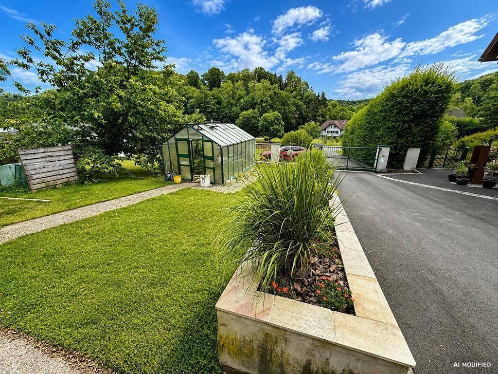 Gepflegter Gartenbereich mit Rasenfläche, Gewächshaus und Zufahrt zum Grundstück.