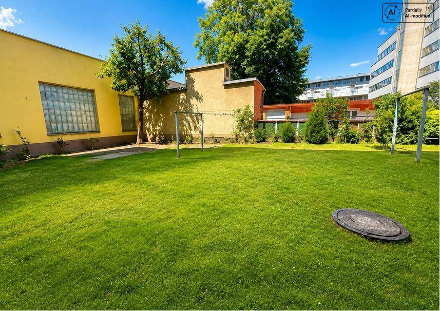Große Rasenfläche im Gemeinschaftsgarten mit umliegenden Gebäuden und Bäumen.