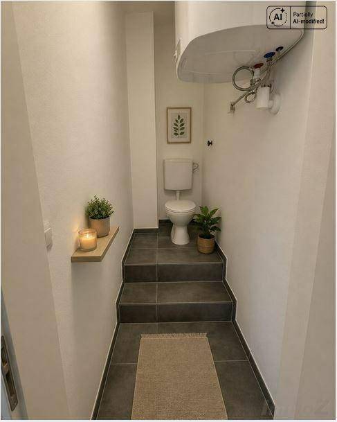 Kleines WC mit dunklen Fliesenstufen, weißer Toilette und minimalistischer Dekoration.