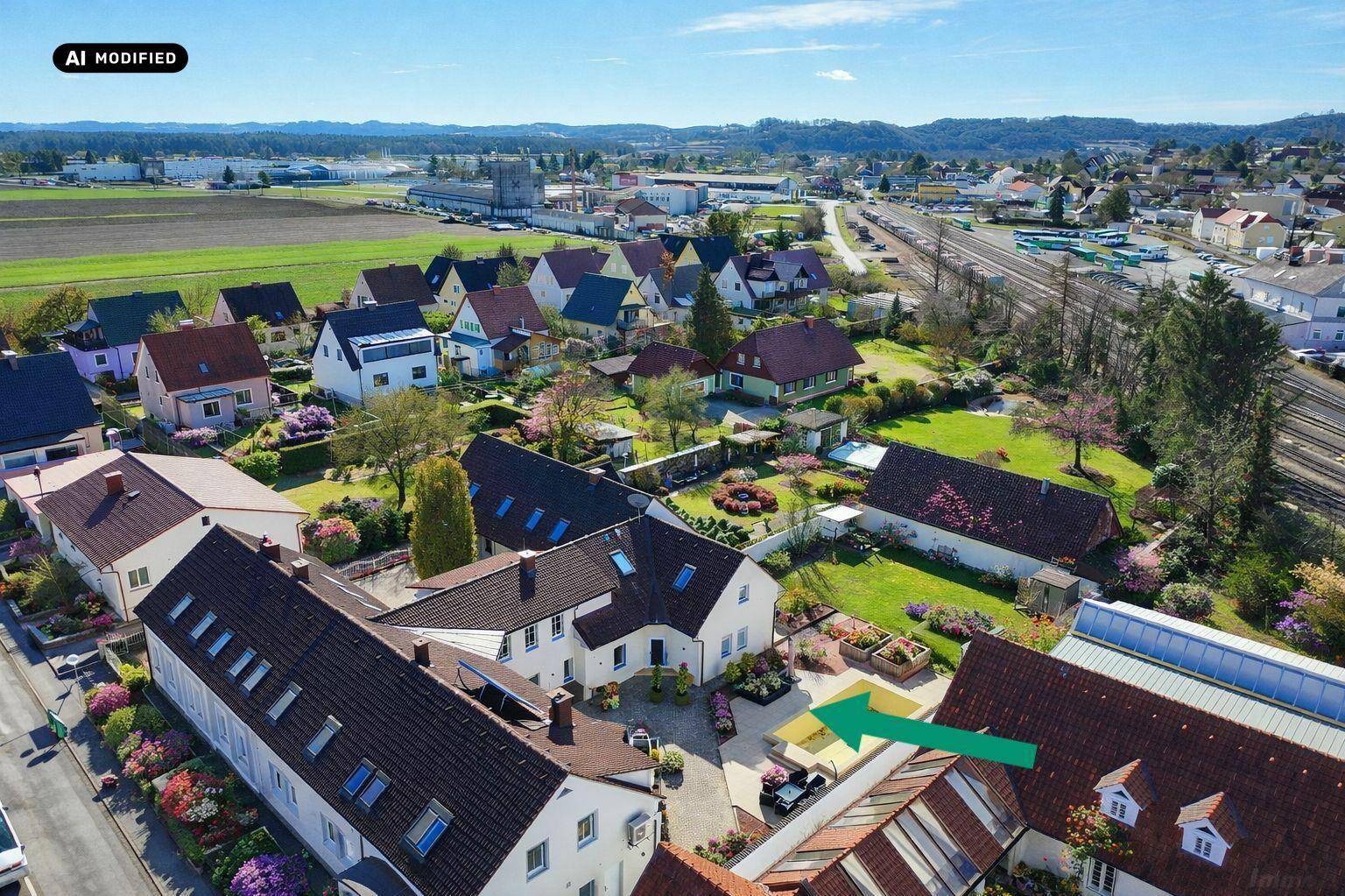 Drohnenaufnahme eines Wohngebiets mit Häusern, Gärten und Bahngleisen im Hintergrund.