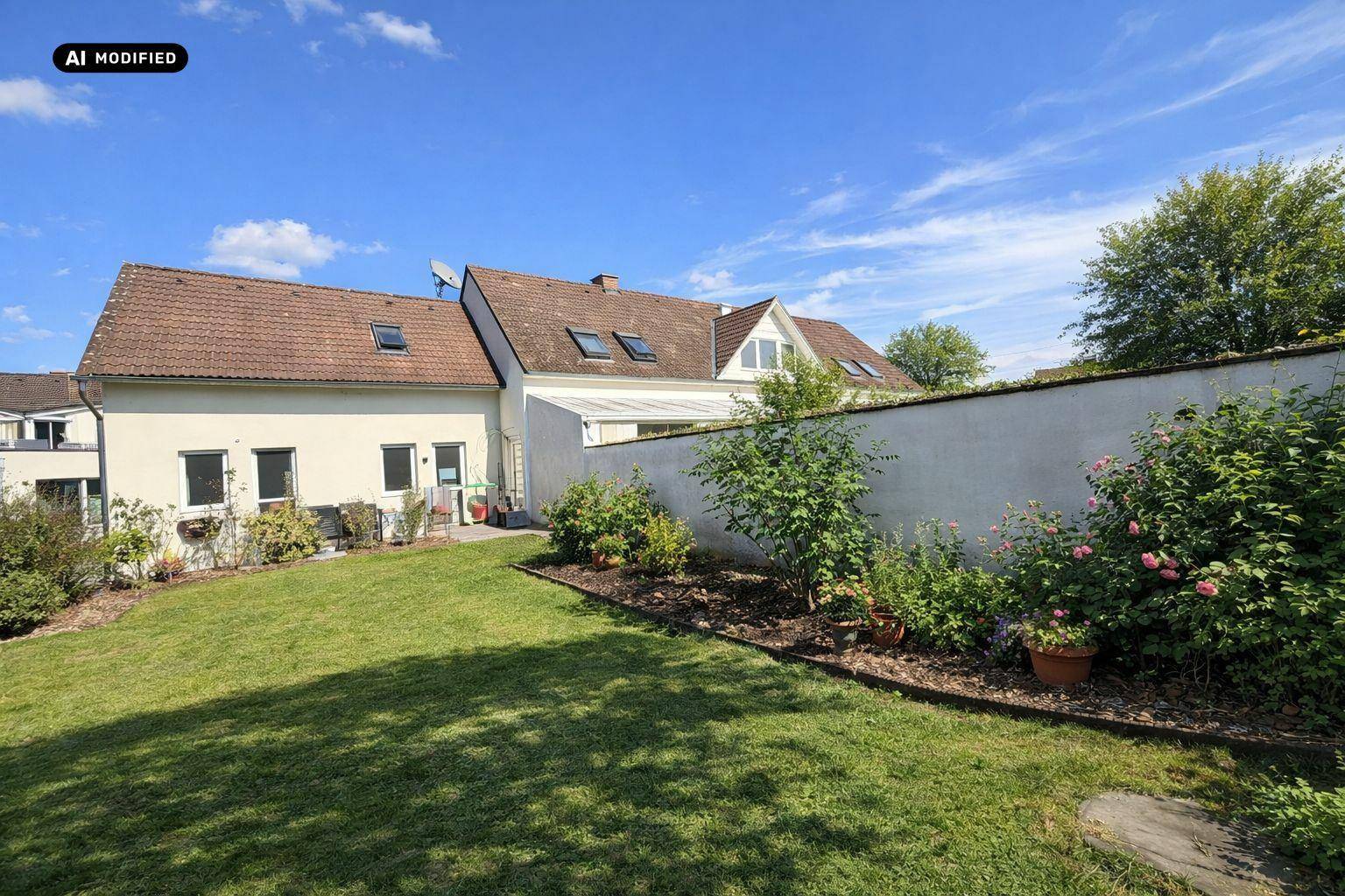 Gepflegter Garten mit Rasenfläche, Blumenbeeten und der Rückseite des Wohnhauses.