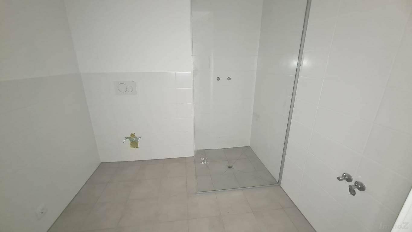 Unmöbliertes Badezimmer mit Fliesenboden und vorbereitetem Bereich für eine Dusche.