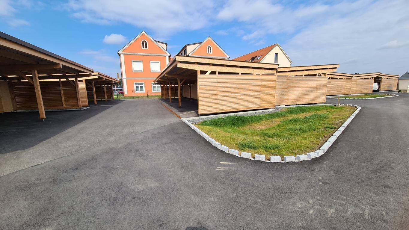 Moderne Carports aus Holz mit angrenzenden Wohngebäuden in ländlicher Umgebung.
