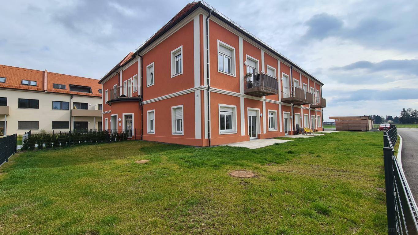 Neubau-Wohngebäude mit oranger Fassade, Balkonen und einer weitläufigen Rasenfläche.