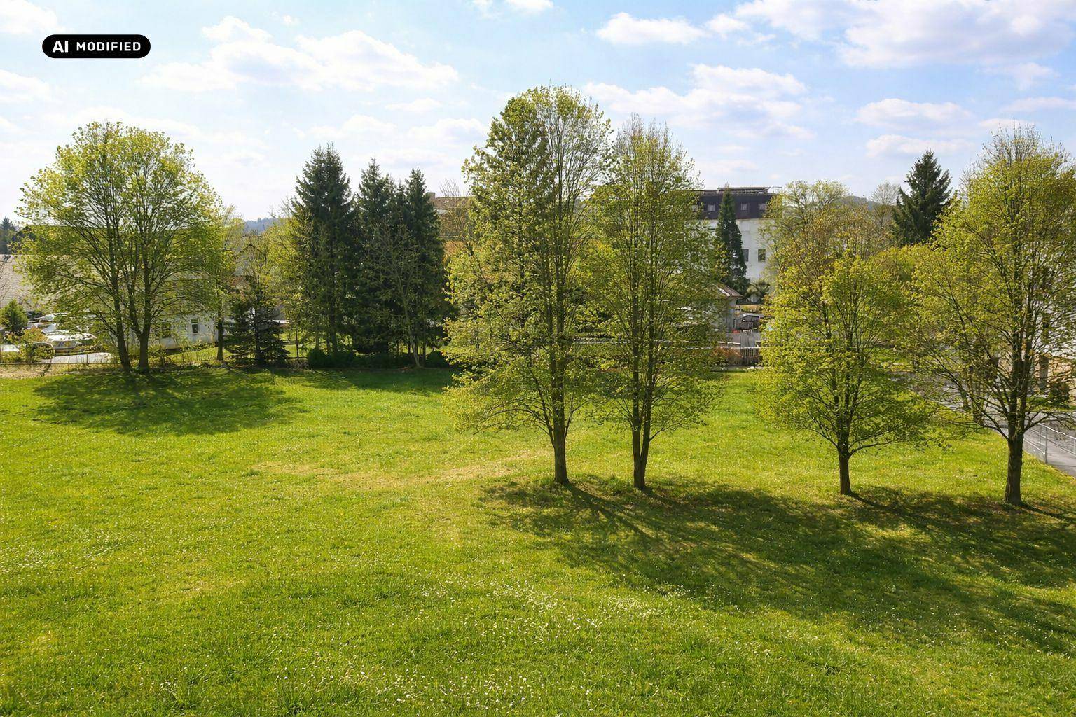 Weitläufige grüne Wiese mit Bäumen unter blauem Himmel, bietet einen idyllischen Ausblick.