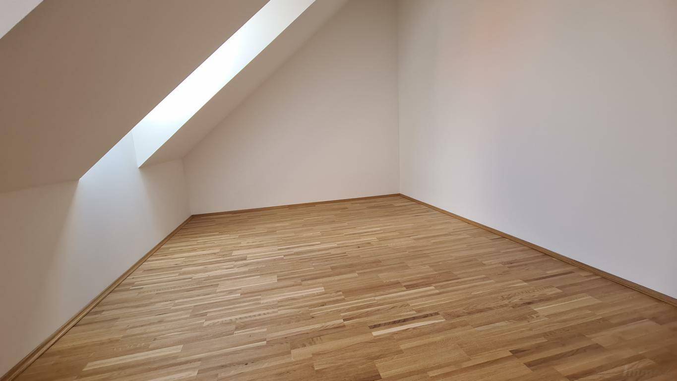 Unmöbliertes Zimmer im Dachgeschoss mit Parkettboden und einem schrägen Dachfenster.