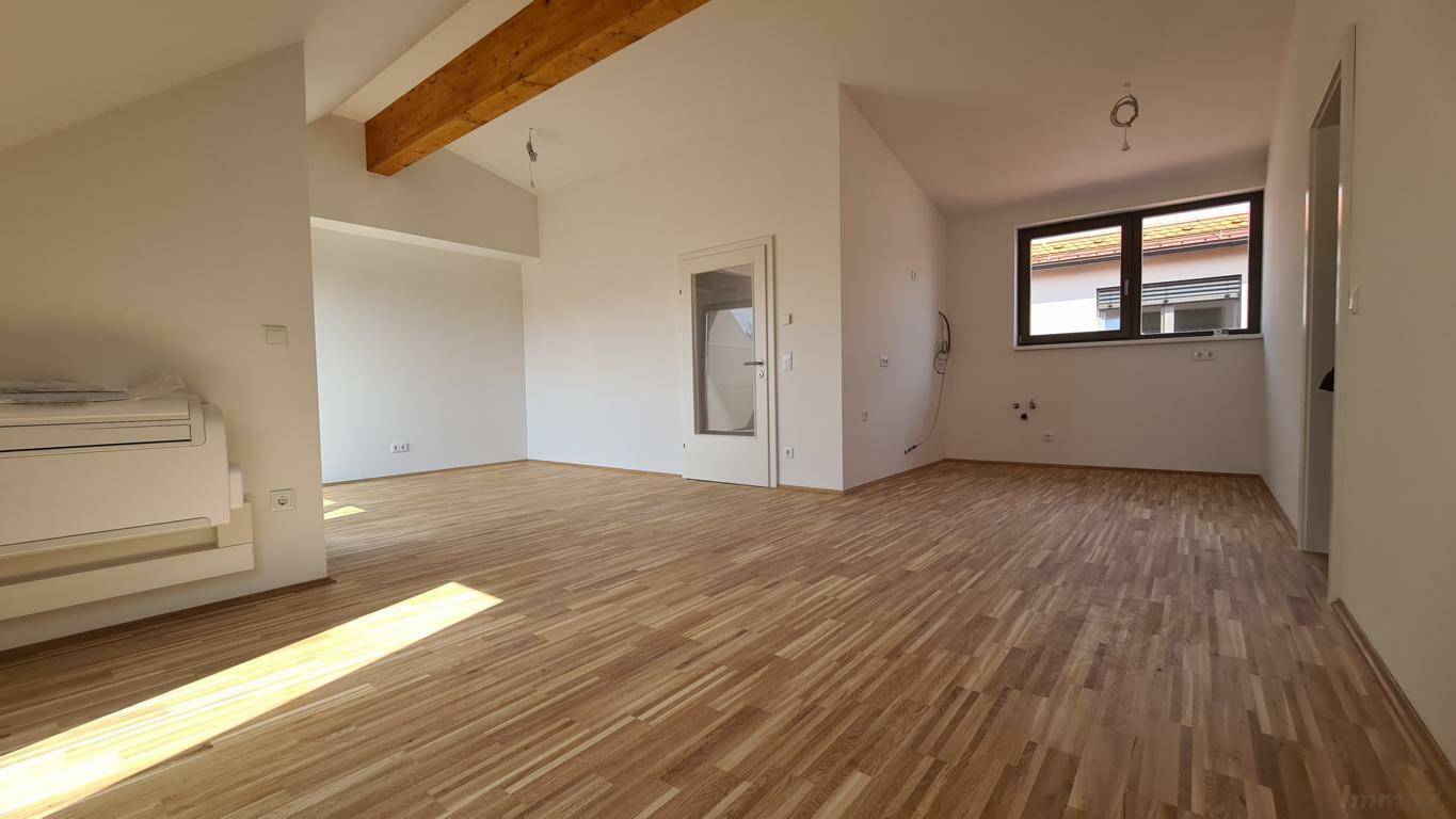 Offener, unmöblierter Wohn- und Küchenbereich im Dachgeschoss mit Parkettboden und Fenster.