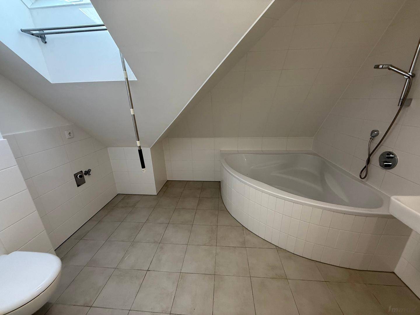Leeres Badezimmer mit Eckbadewanne, Dusche, Fliesenboden und Dachfenster.