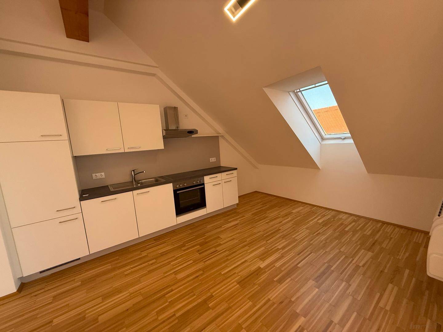 Funktionale Einbauküche mit weißen Schränken und Dachfenster in einem hellen Raum.