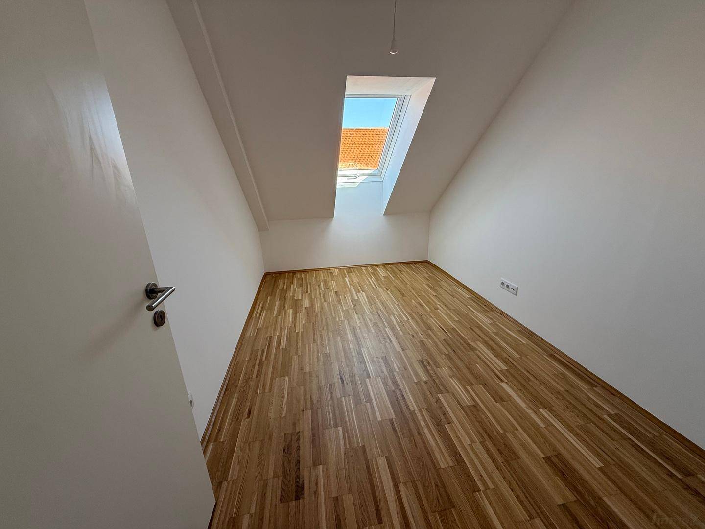 Heller Raum im Dachgeschoss mit Parkettboden und Dachfenster, ideal als Ankleidezimmer.