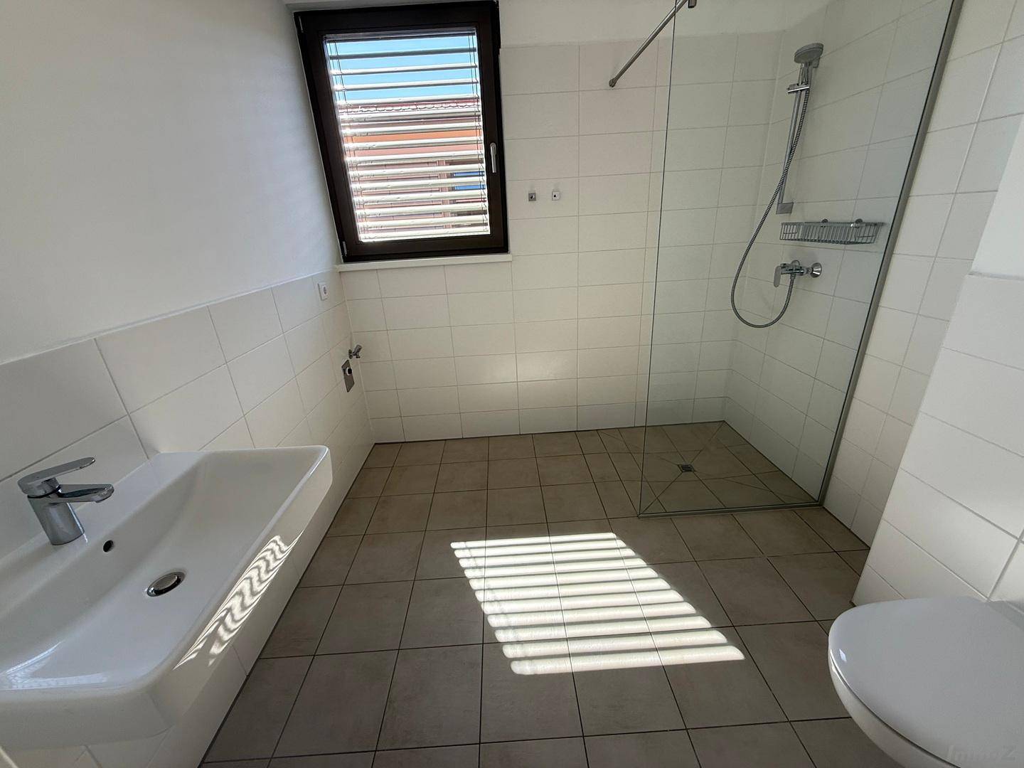 Helles Badezimmer mit Dusche, WC, Waschbecken und Fenster, bereit zur Einrichtung.