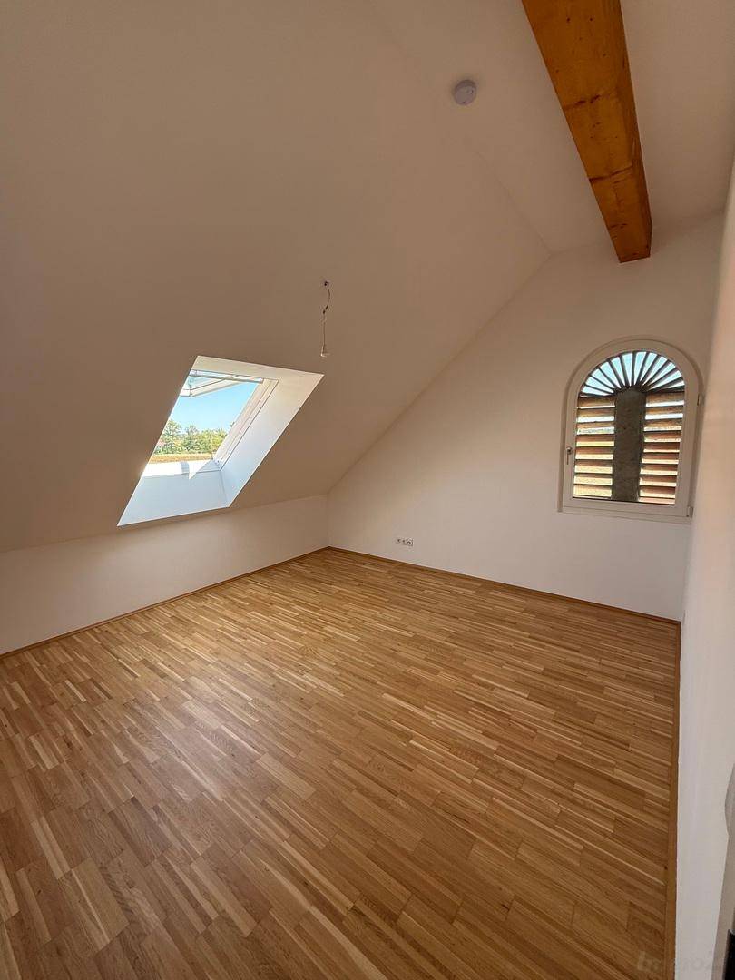 Leeres Schlafzimmer im Dachgeschoss mit Parkettboden, Holzbalken und Dachfenster.