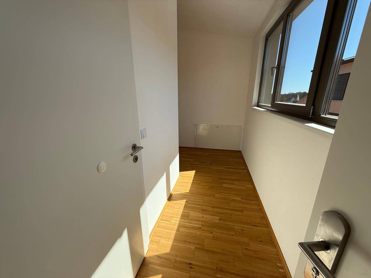 Heller Flur mit Parkettboden und großen Fenstern, die viel Tageslicht hereinlassen.