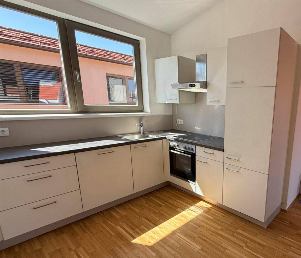 Funktionale Einbauküche mit hellen Fronten, dunkler Arbeitsplatte und Holzparkettboden.