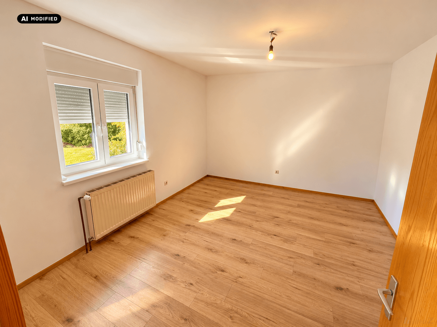 Heller Raum mit Holzboden, weißen Wänden und Fenster mit Blick ins Grüne, unmöbliert.