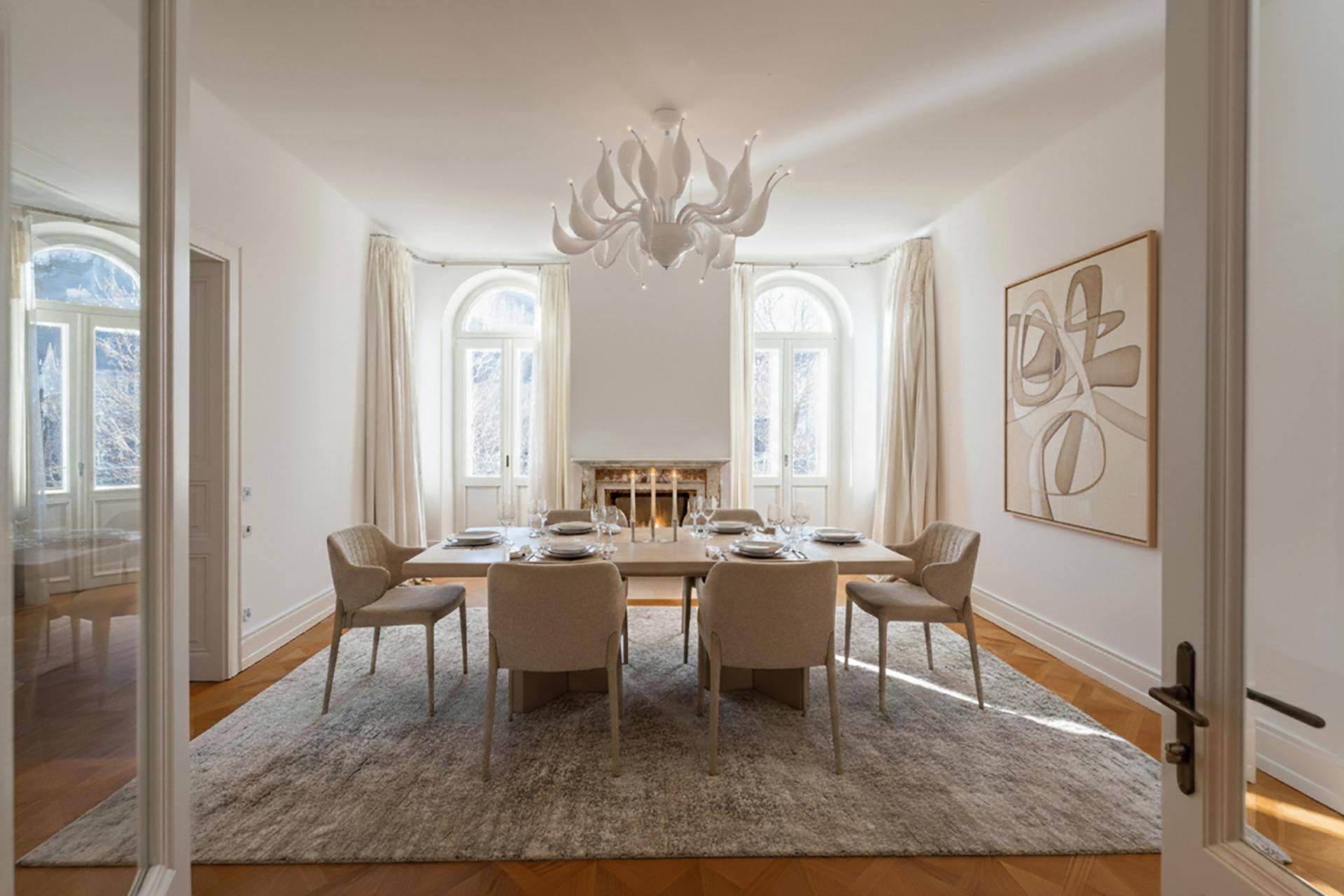 Eleganter Essbereich mit stilvollem Kronleuchter, Kamin und großen Bogenfenstern, die viel Licht hereinlassen.