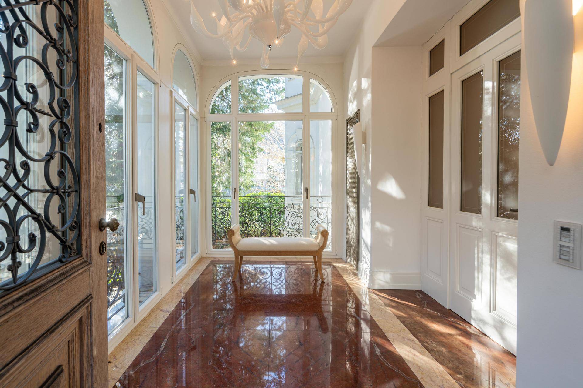 Heller Eingangsbereich mit glänzendem Marmorboden, großen Bogenfenstern und einer kunstvollen Eingangstür.