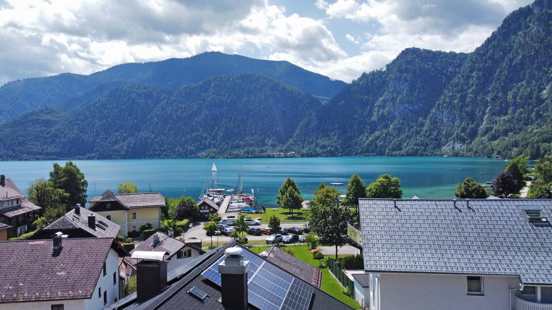 Panoramablick auf einen malerischen See, umgeben von bewaldeten Bergen und einem charmanten Dorf.