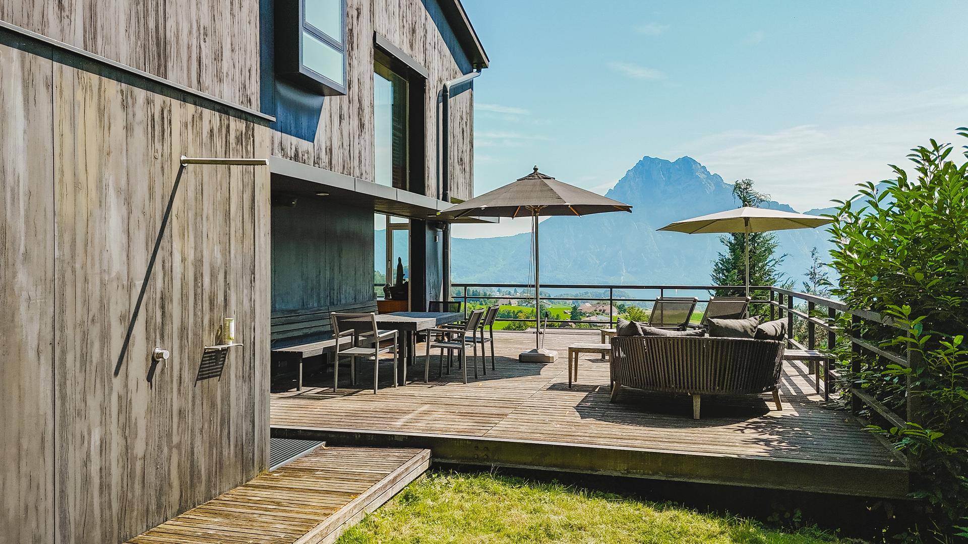 Geräumige Holzterrasse mit Sitzgelegenheiten und Sonnenschirmen, bietet einen atemberaubenden Bergblick.