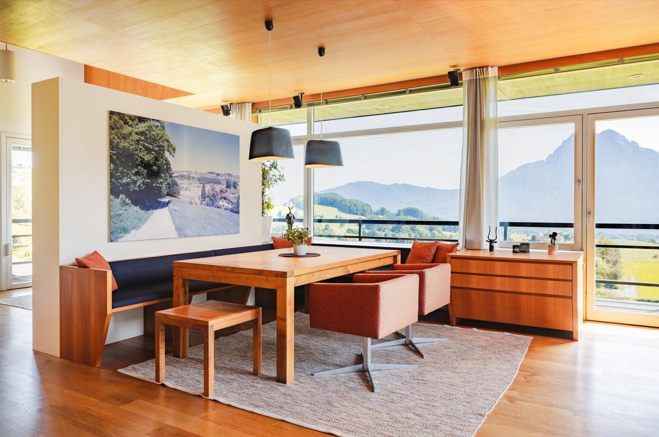Moderner Essbereich mit Holztisch und Sitzbank, umgeben von großen Fenstern mit Bergblick.