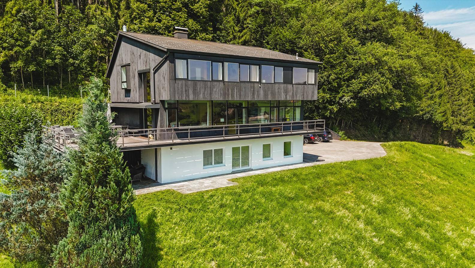 Moderne Architektur mit dunkler Holzfassade und großen Fensterfronten, eingebettet in die Natur.