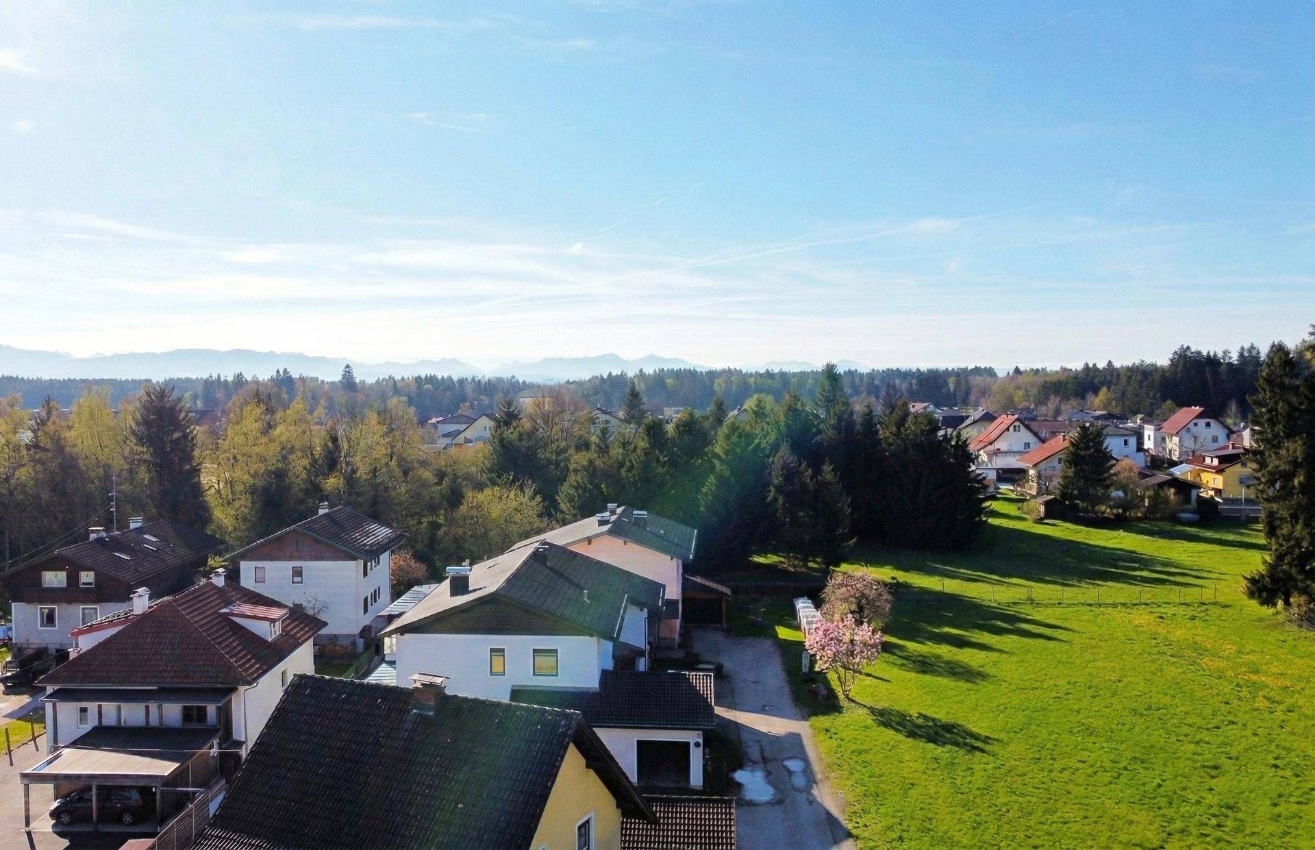 Weitläufige Luftaufnahme einer Wohnsiedlung mit grünen Flächen und Bergen im Hintergrund.