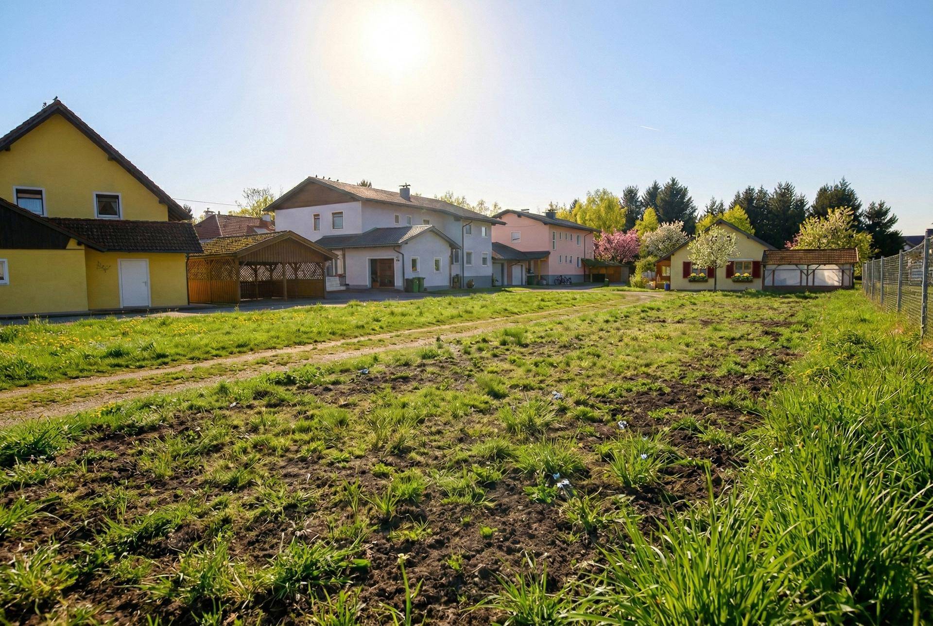 Weitläufiges Grundstück mit Gras und Erde, umgeben von verschiedenen Wohnhäusern unter strahlendem Himmel.